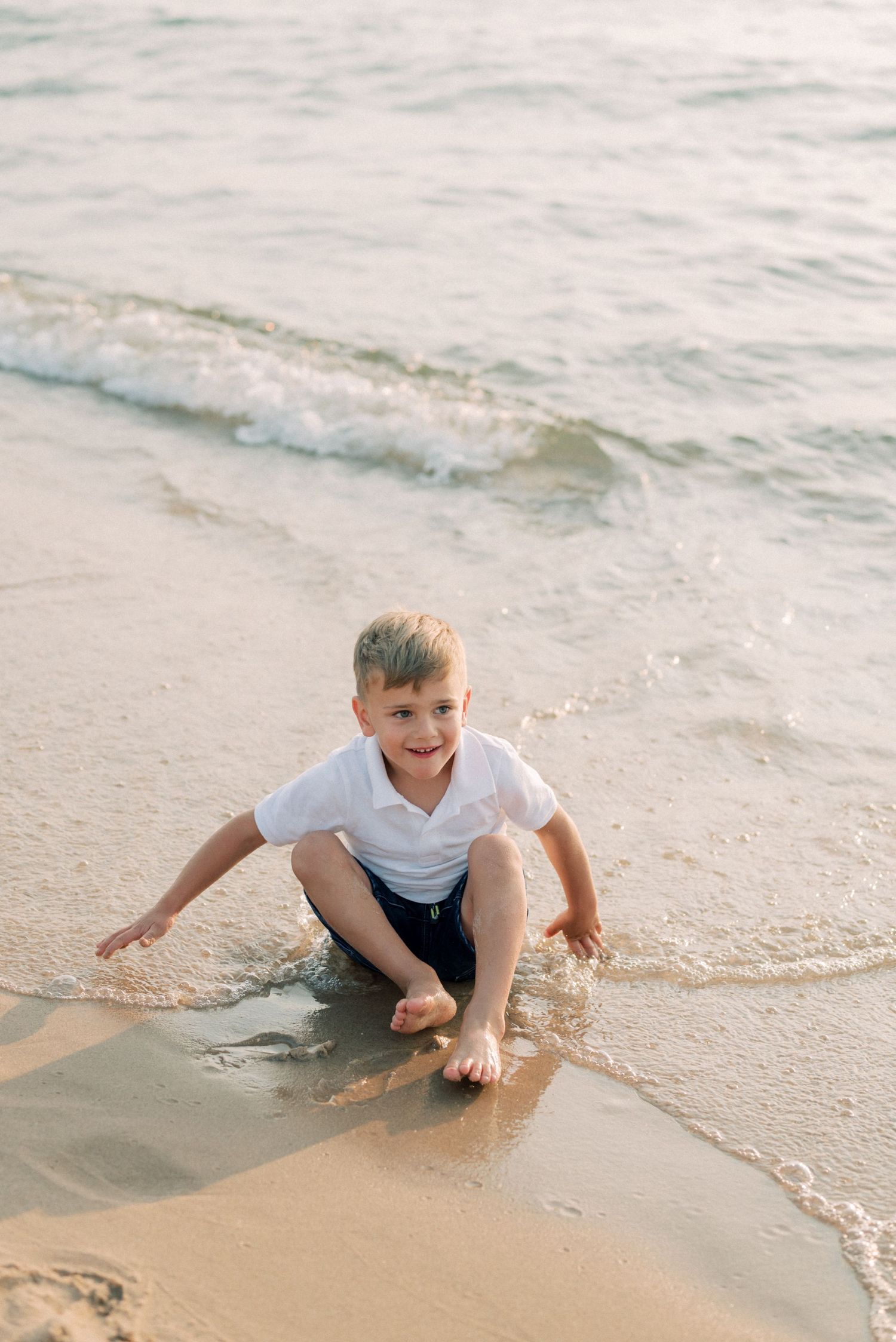 Young child playing in the gentle surf at the water's edge on a sandy beach.
