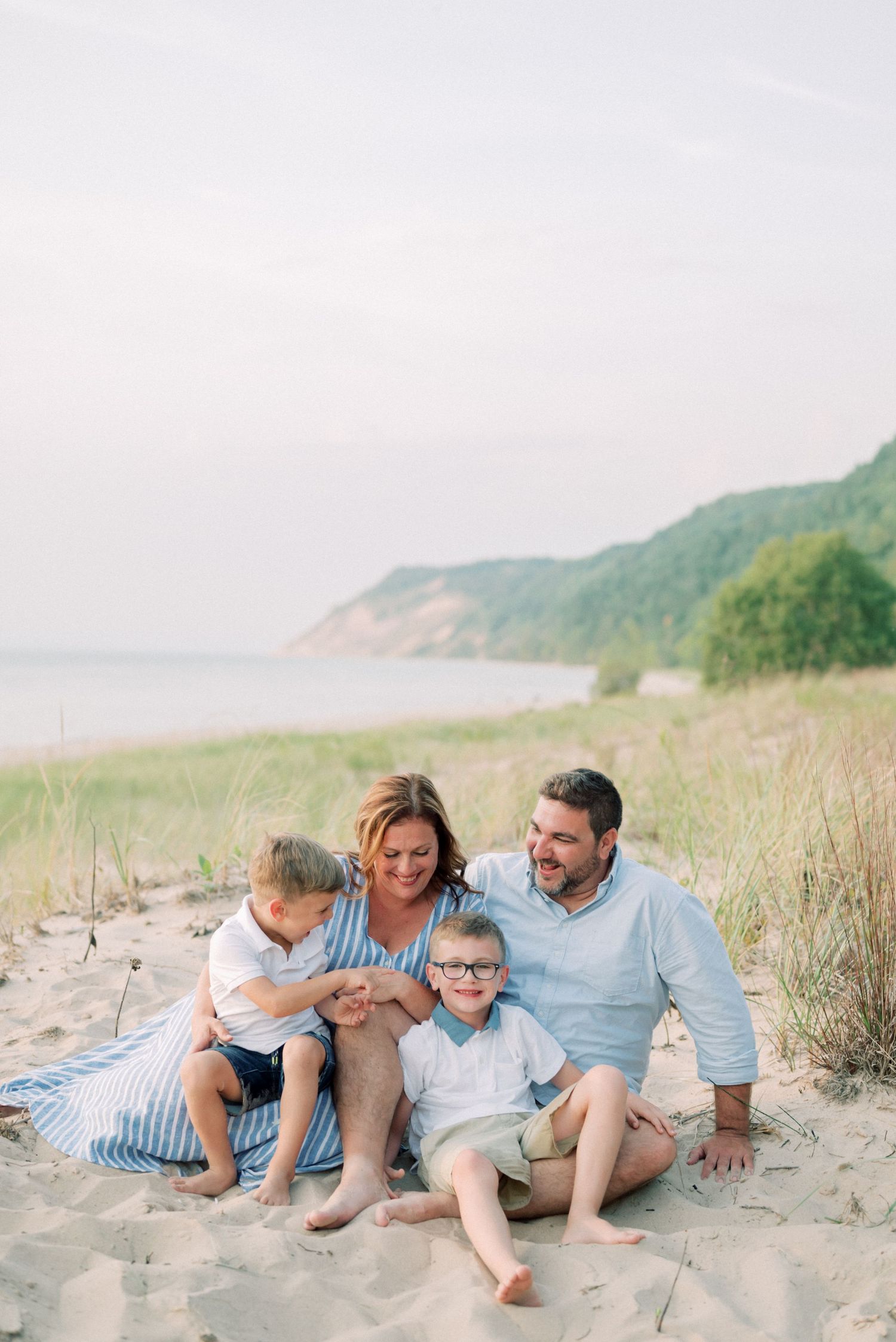 A family sits together on a sandy beach with coastal cliffs and water in the background.