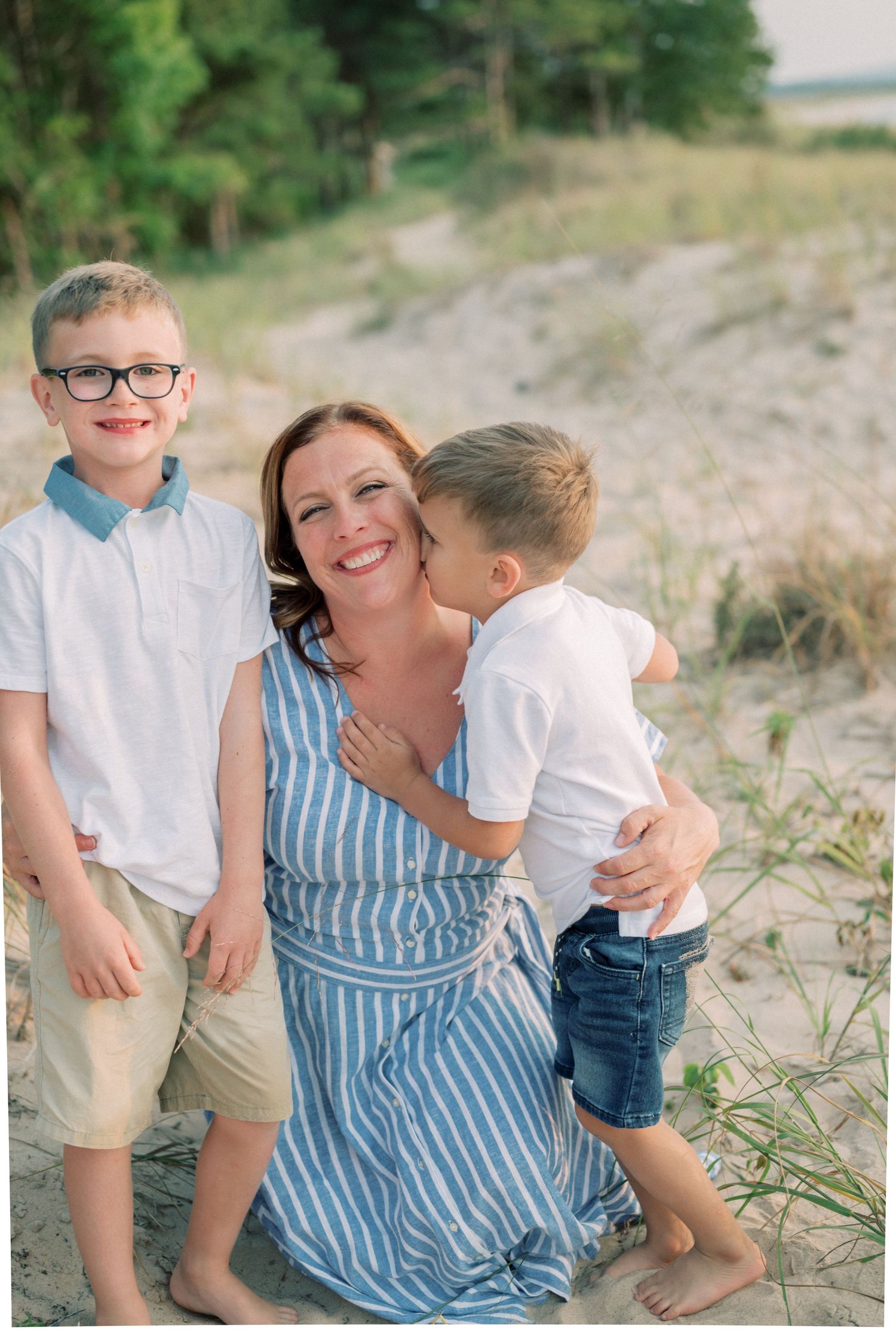 Candid family moment captured on sand dunes with natural foliage in the background.