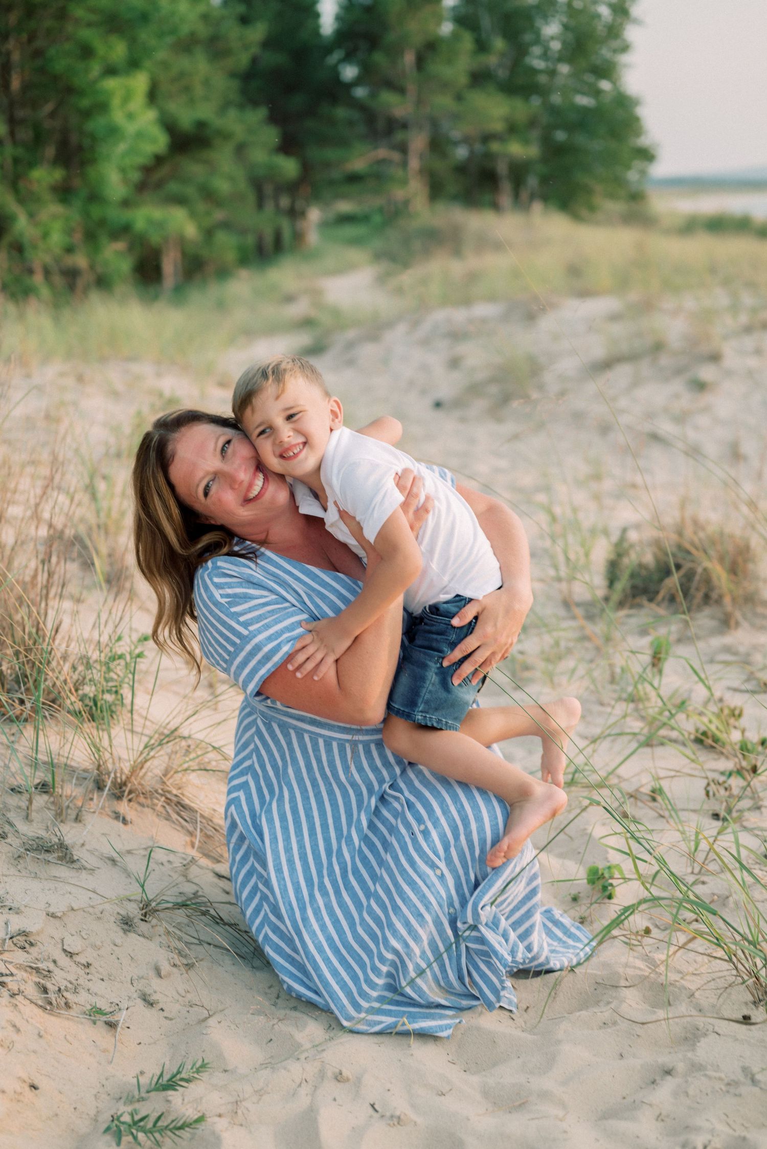 Joyful embrace on a sandy beach path with vegetation and water in the distance.