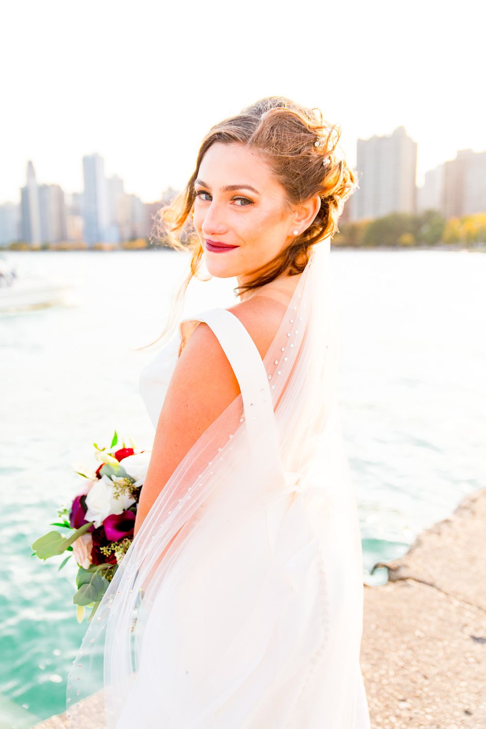 bride lets her veil blow in the wind in front of chicago cityscape
