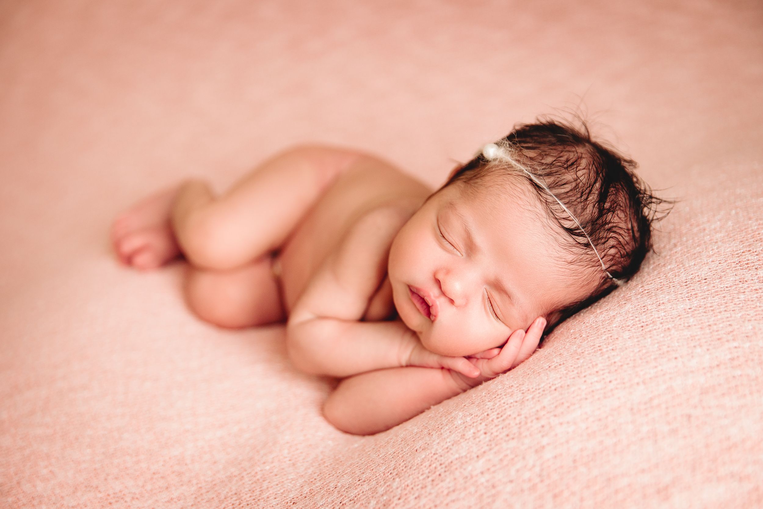 baby girl sleeping on pink blanket hands under cheek