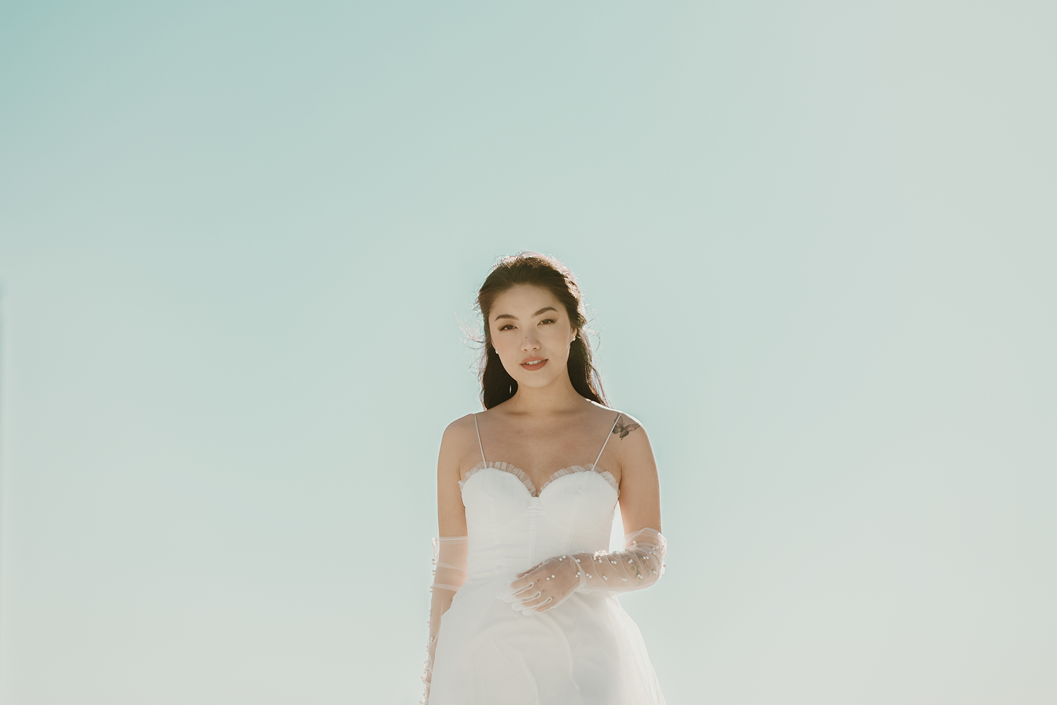 A bridal portrait showing an elegant white wedding dress against a light blue sky background.