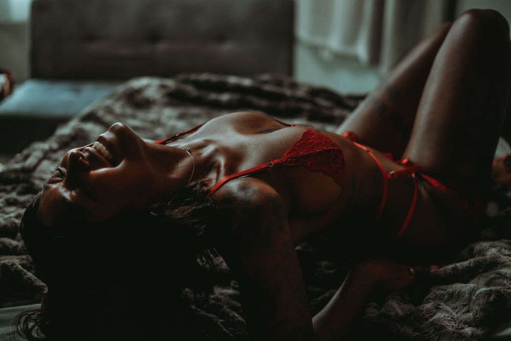 dark skinned woman arching her back on a bed and grinning, wearing red lingerie set