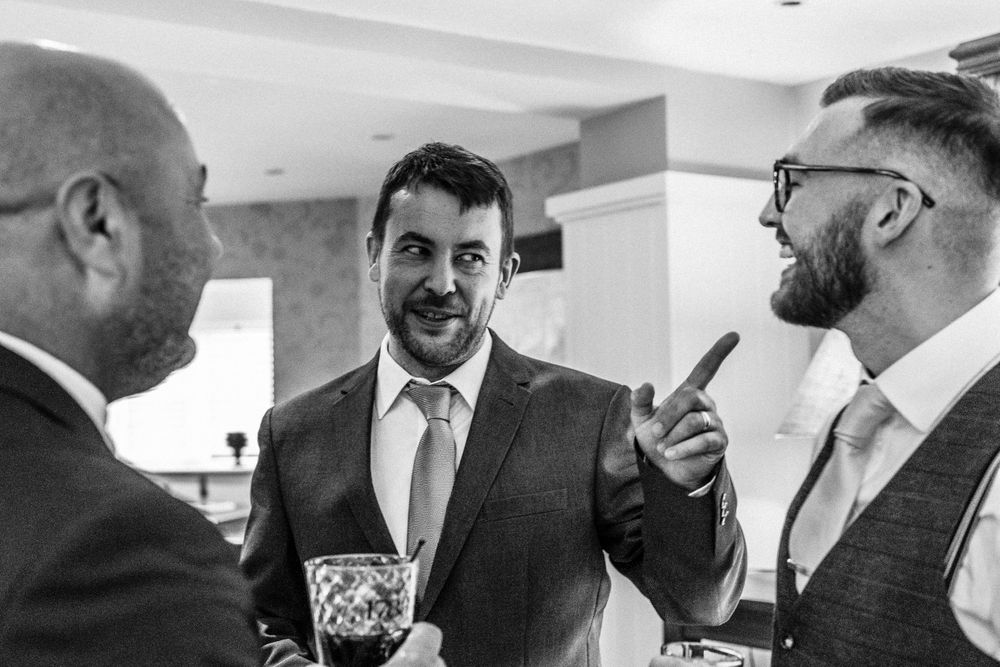 Black and white photo of groom laughing with guests