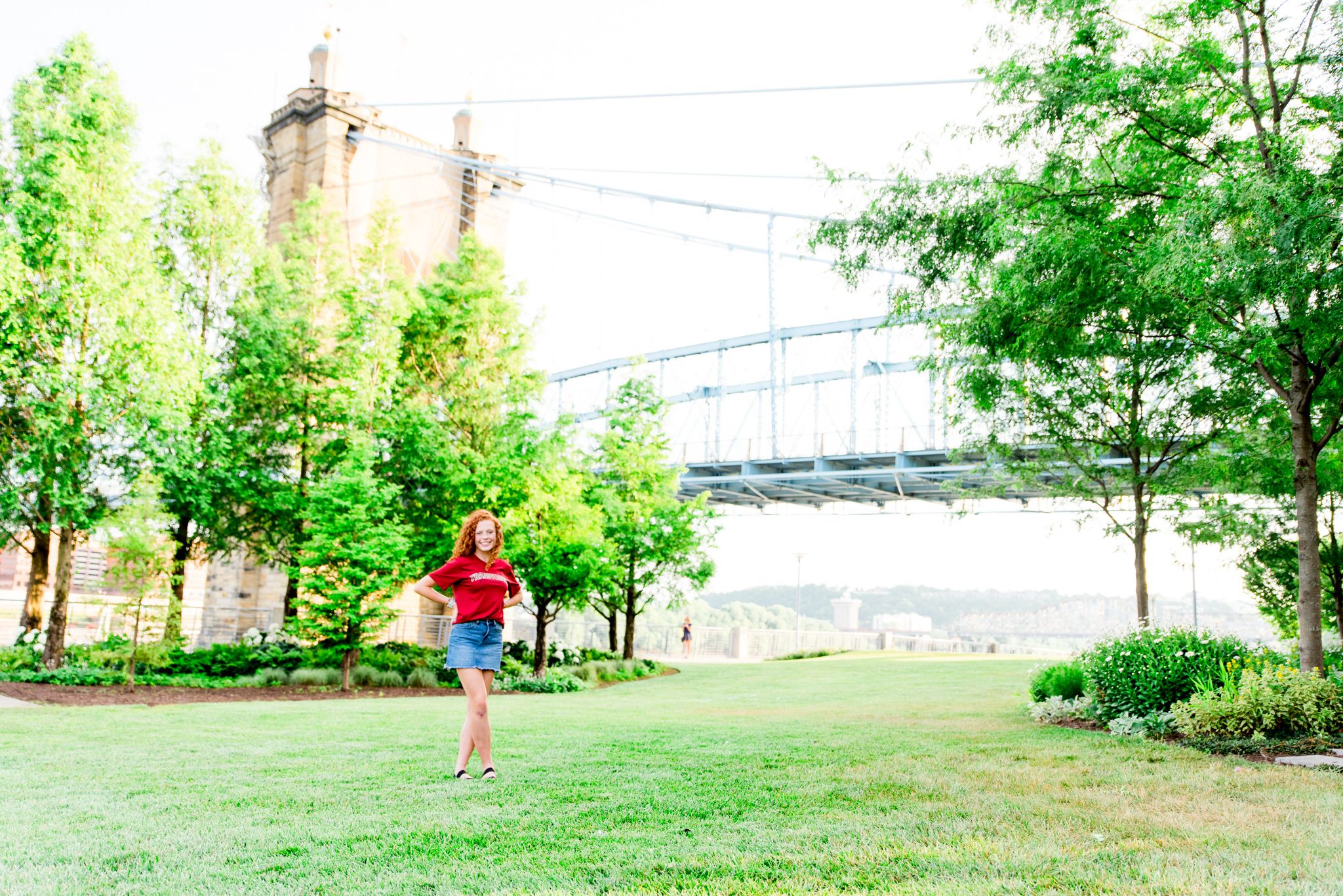 young woman in red Transylvania shirt standing in Smale Park in front of the Roebling Bridge