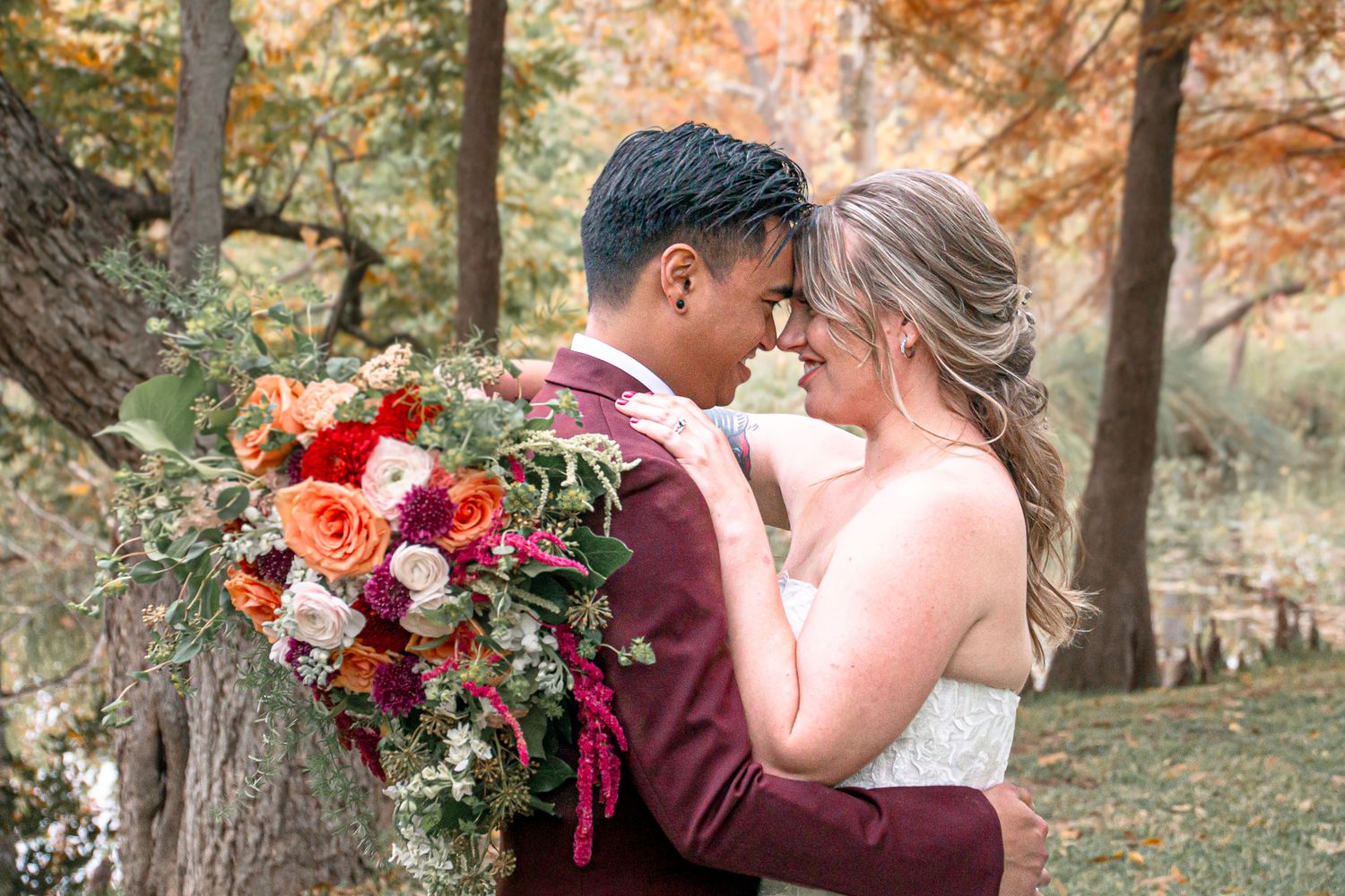 A romantic wedding moment in a forest setting with a vibrant burgundy and coral bouquet.