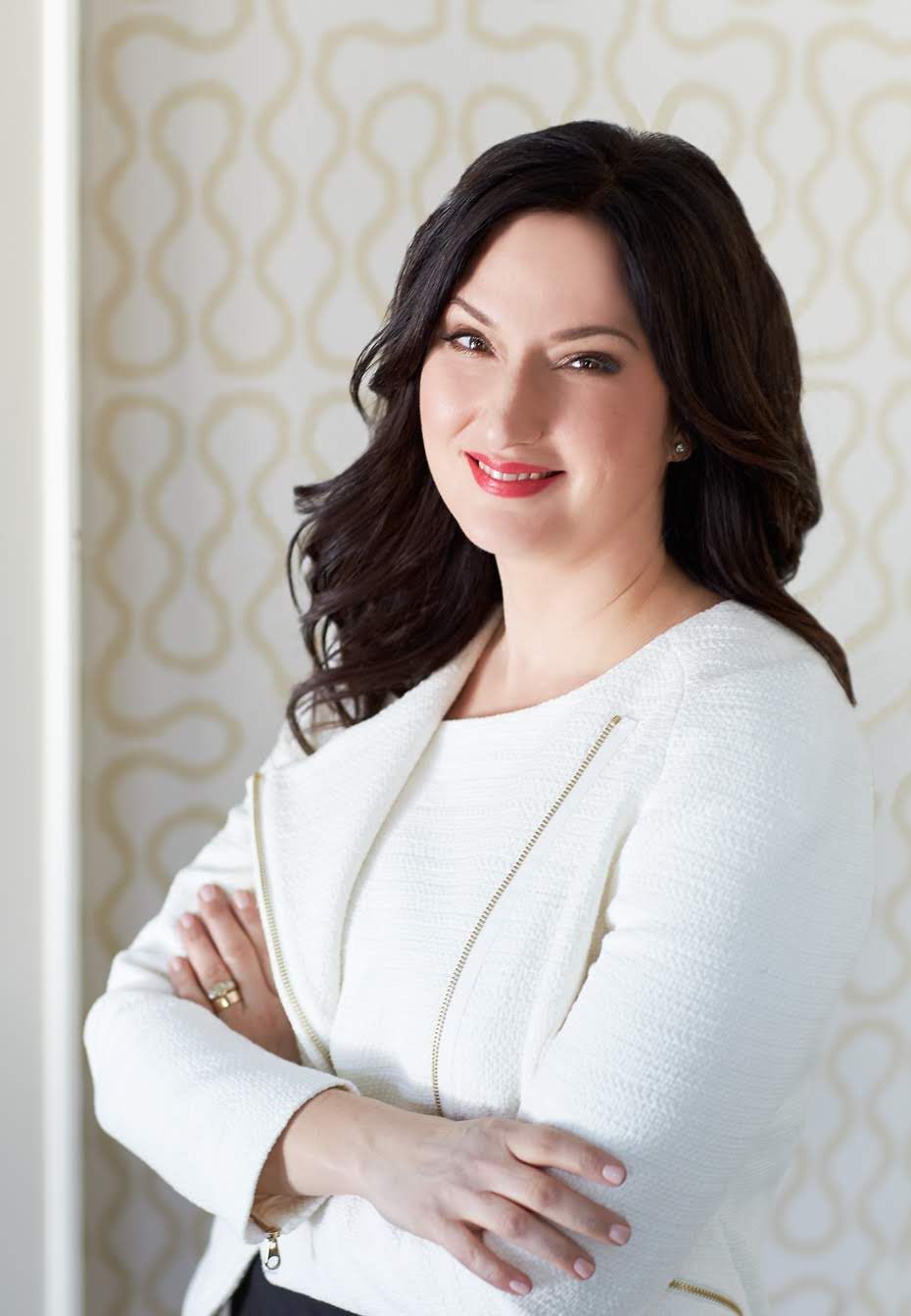 Professional portrait in white blazer against patterned wallpaper.