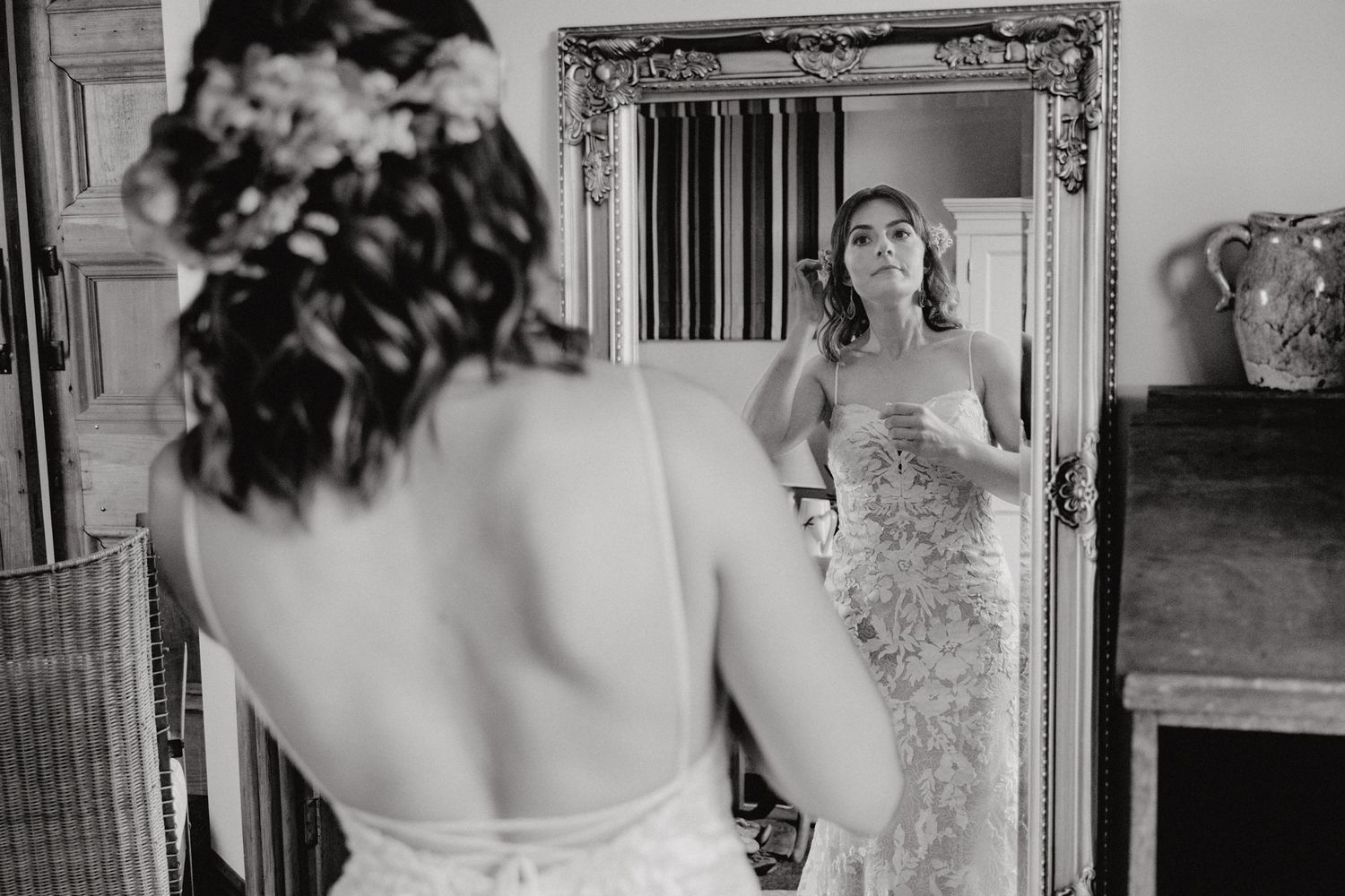 Black and white photo of someone admiring their reflection in an ornate mirror while wearing a wedding dress.