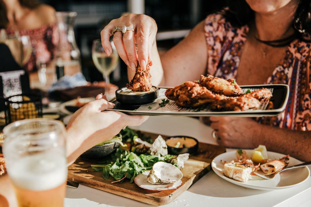 plate of chicken wings with one being dipped in sauce by lady