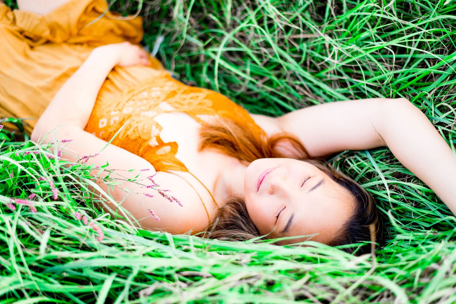 young woman in yellow lace dress laying in green grass with eyes closed