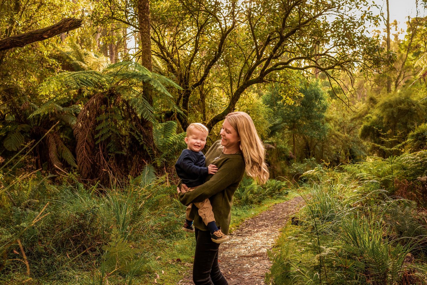 Mother with long hair and toddler in her arms spinning in a circle in the forest outside Melbourne