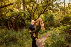 Mother with long hair and toddler in her arms spinning in a circle in the forest outside Melbourne