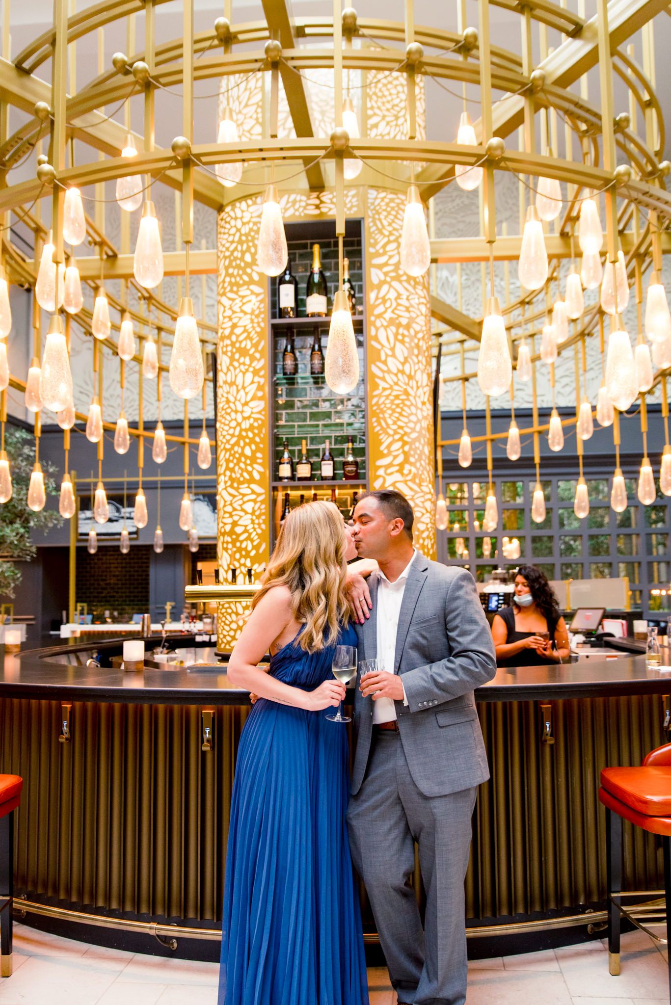 young engaged couple in blue and grey kissing in front of gold chandelier at Lytle Park Hotel bar