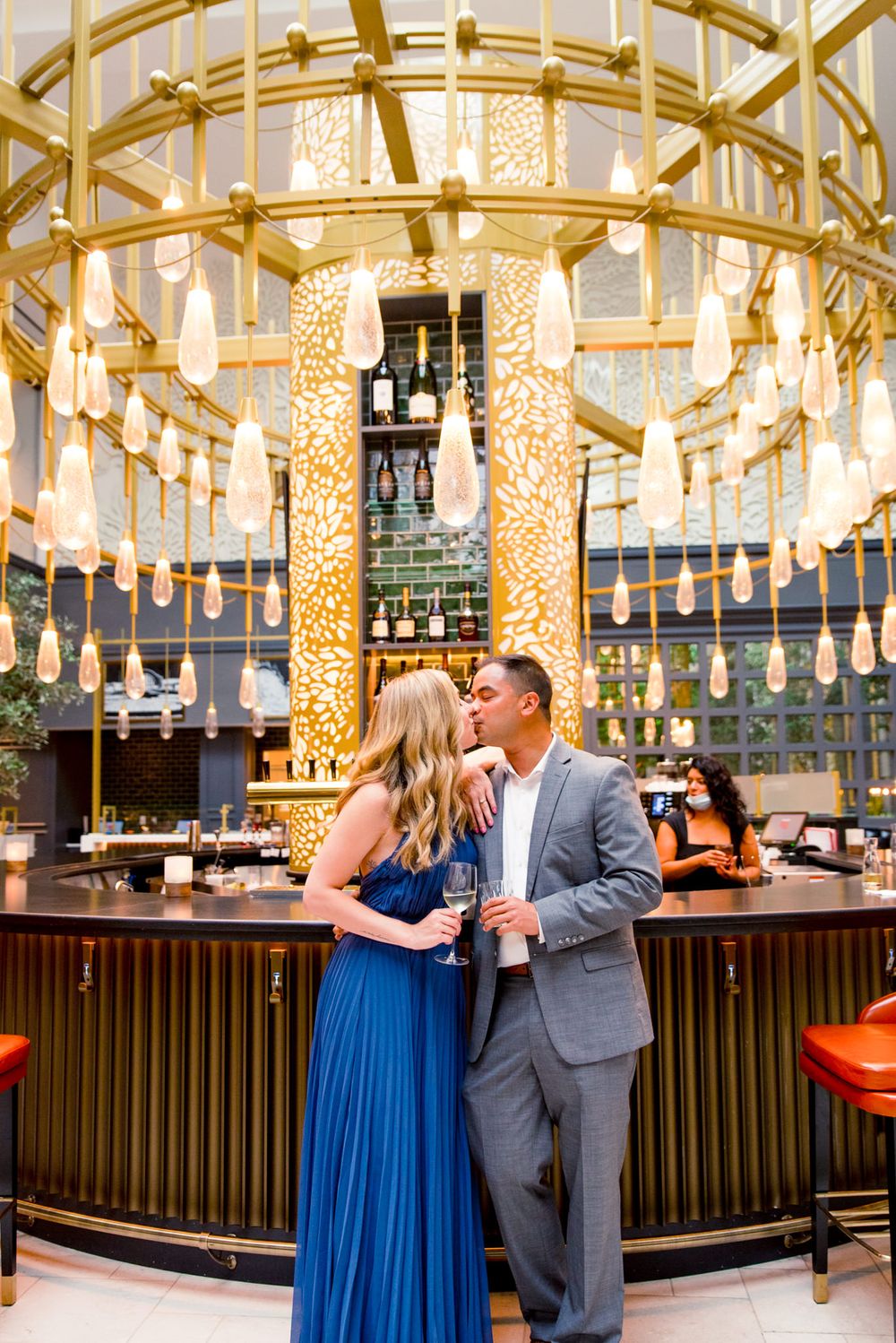 young engaged couple in blue and grey kissing in front of gold chandelier at Lytle Park Hotel bar