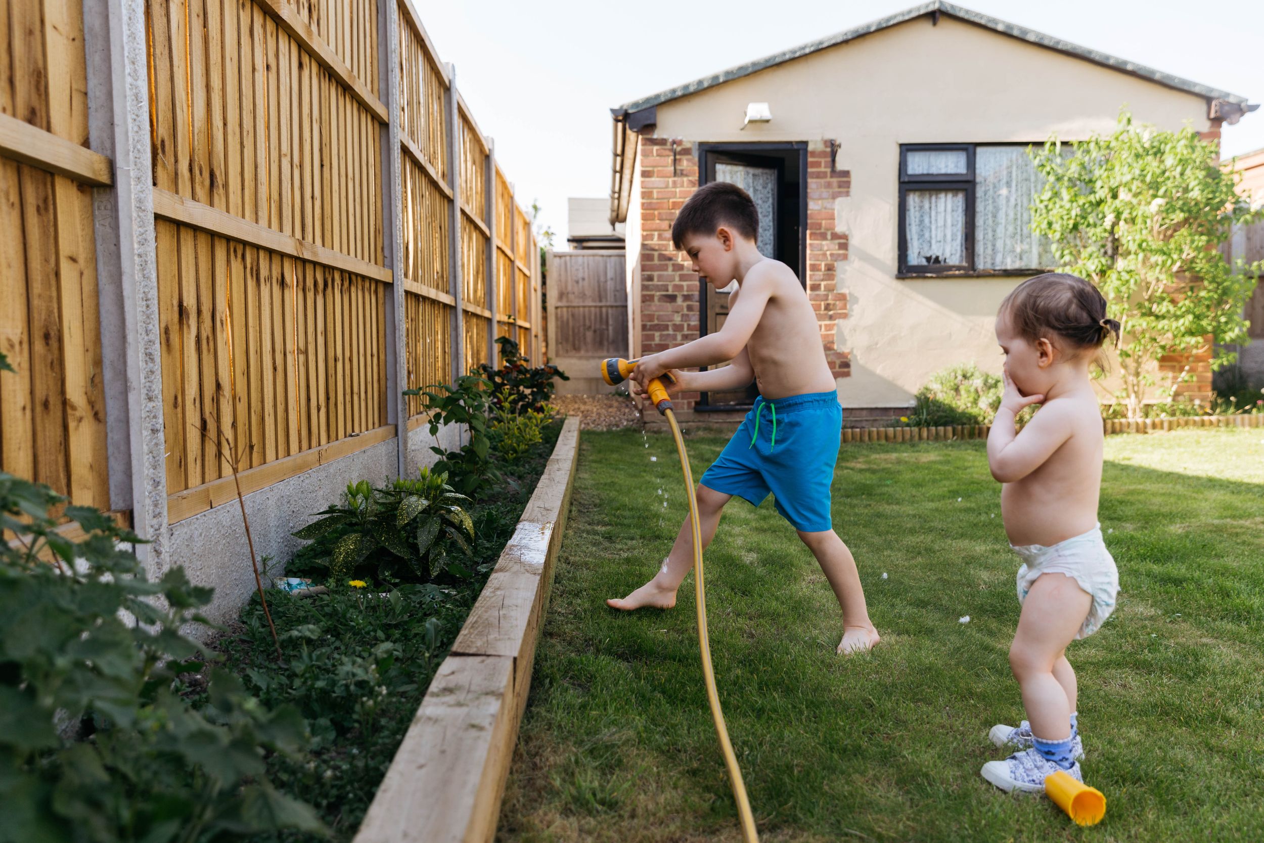 two kids watering garden plants with hose