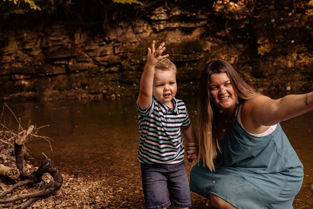 young boy in blue splashing in the creek with his mom in imperial mo with st louis family photographer
