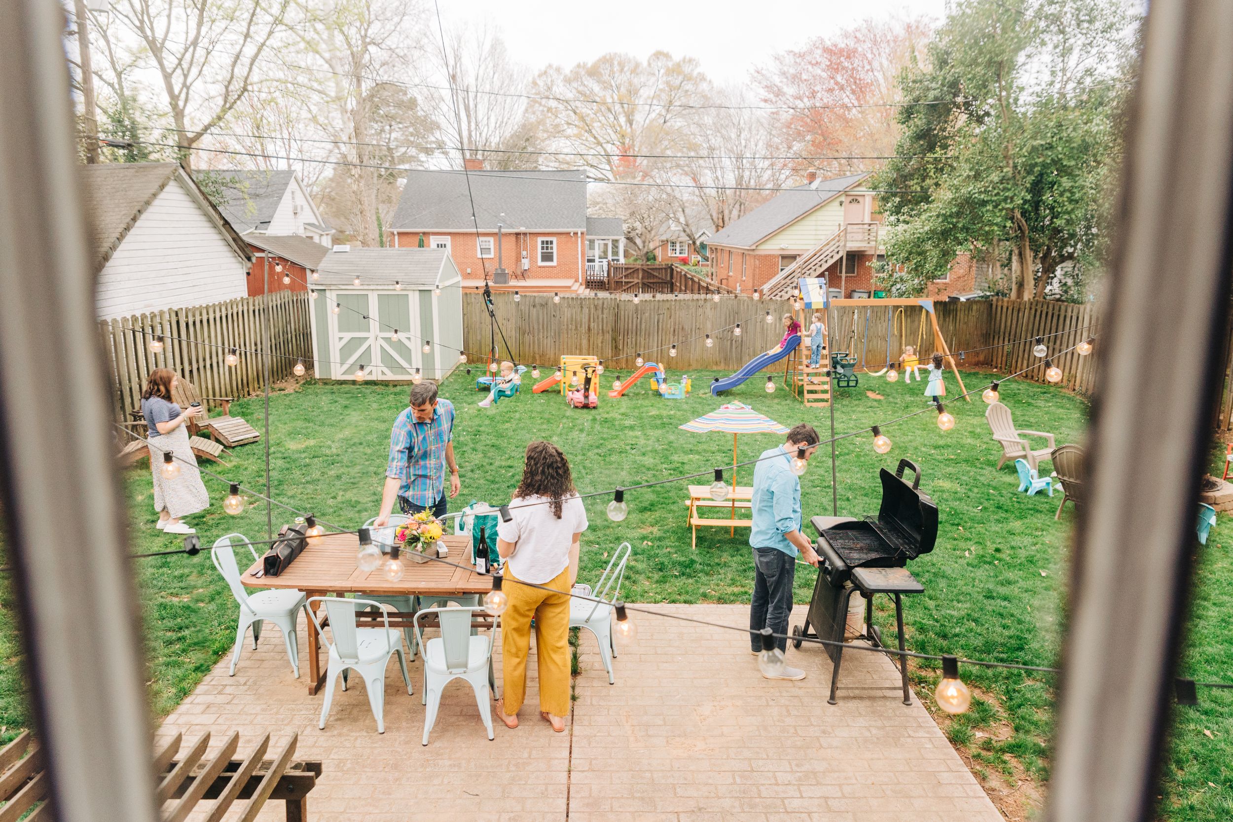 Two families are spread out in a Charlotte backyard playing and cooking during a barbecue