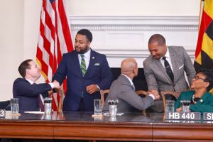 Governor Wes Moore, News Anchor Darren Haynes and officials engaged in discussion during a legislative session with American flag displayed.