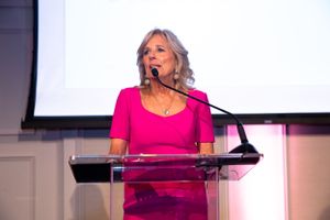 FLOTUS Jill Biden speaking at podium wearing bright pink dress at formal event.