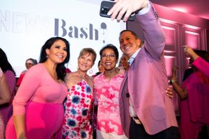 Four attendees taking selfies together at an event with pink lighting and Bash branding. with News Anchors