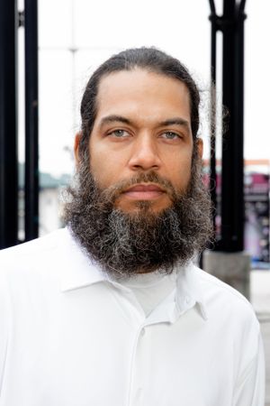 Portrait of man with full beard wearing white shirt against urban background.