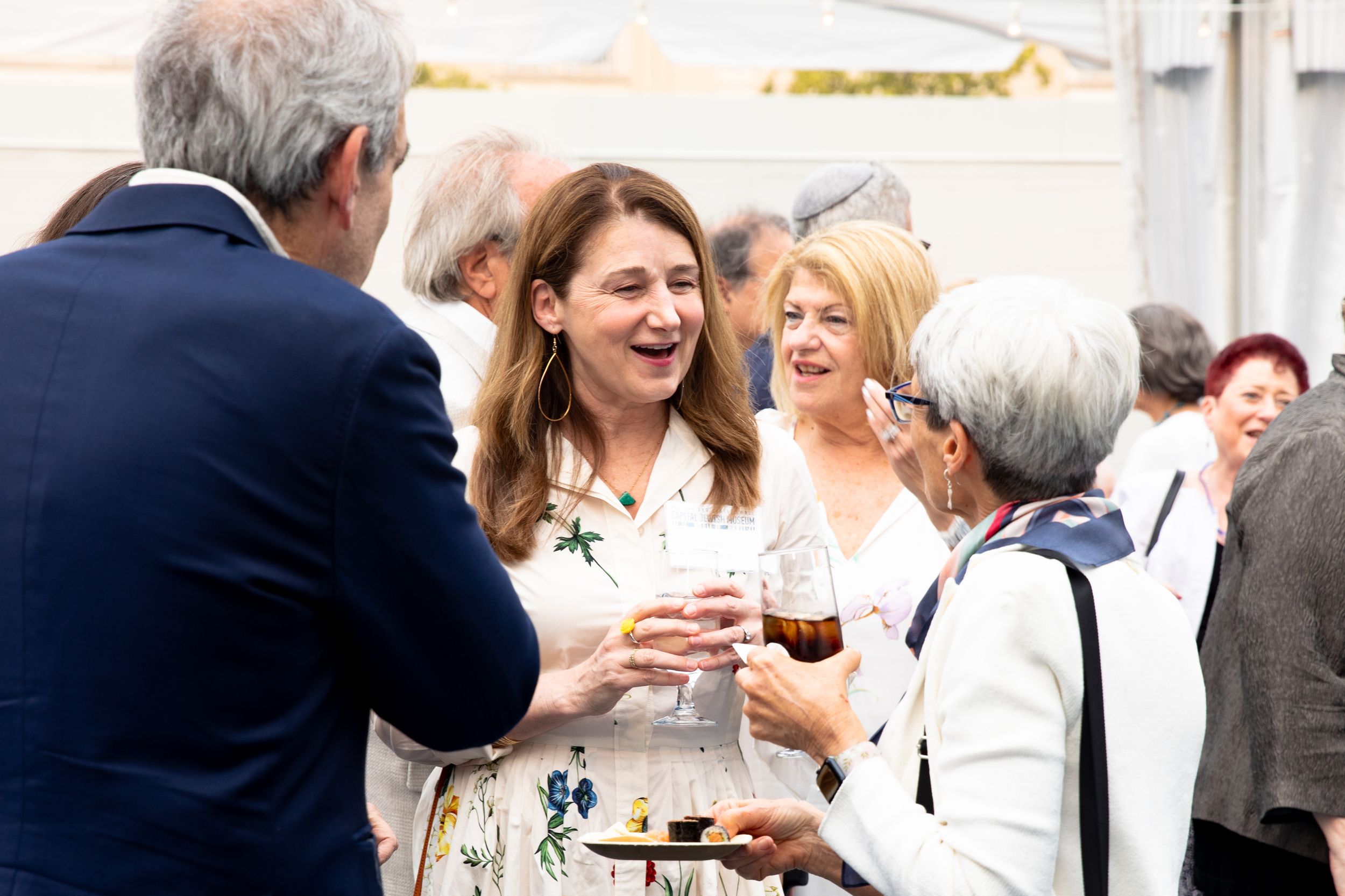 A group of people laugh and socialize while enjoying wine at an outdoor event.