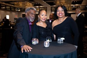 Three guests smile while gathered around cocktail table at formal evening event.