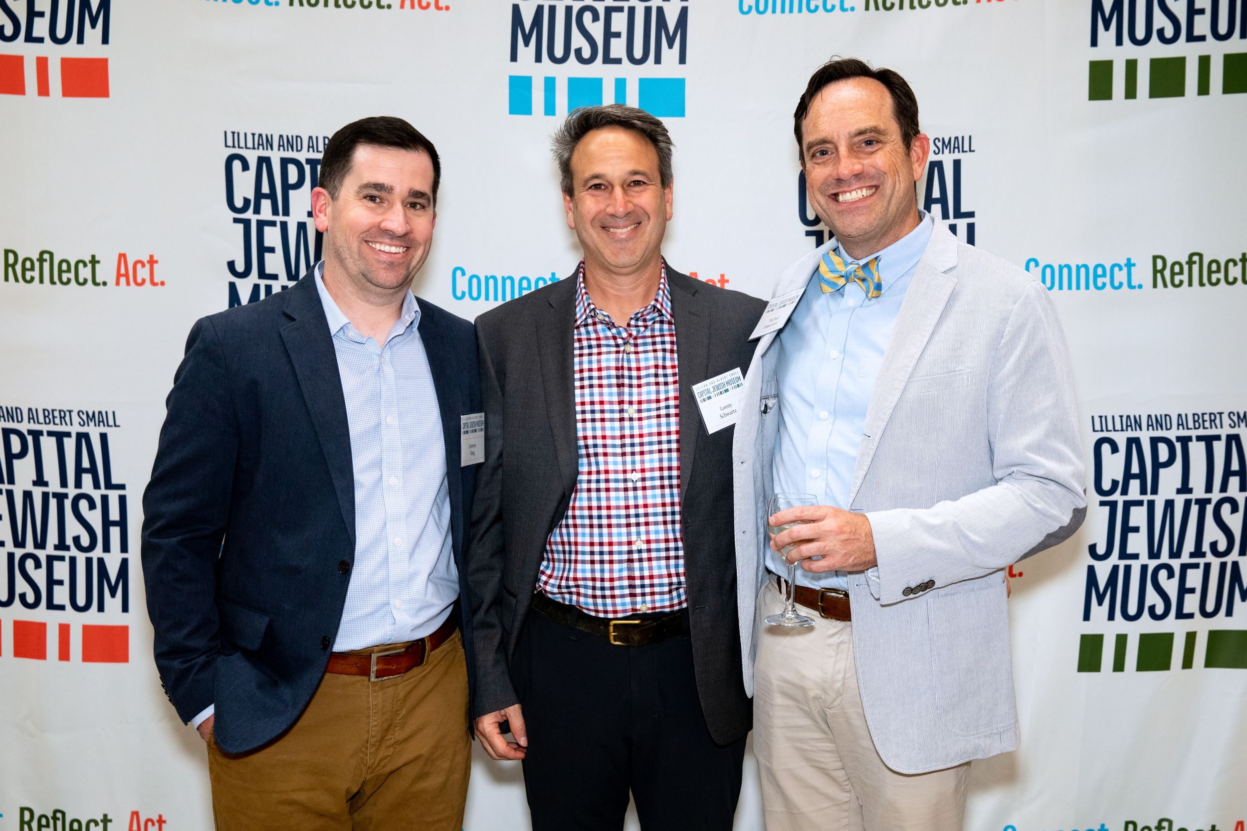 Three men in business attire pose together at a museum event.
