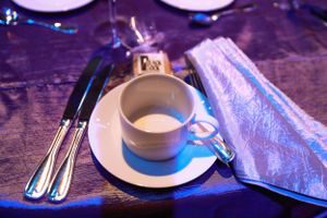 Coffee cup and silverware set on dark blue table with moody lighting.