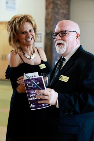 Two attendees at formal event holding auction catalogs and smiling.