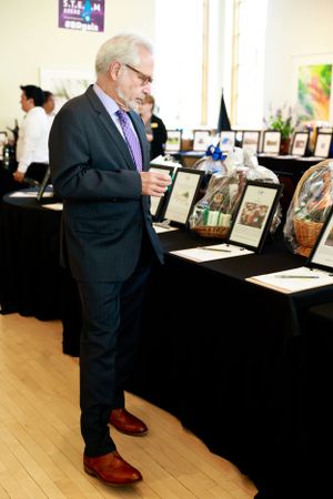 Attendee in navy suit examining items displayed on black-draped table at auction event.