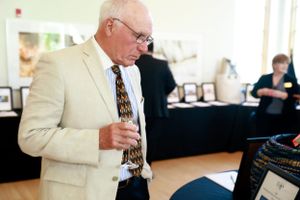 Senior attendee in light suit viewing items at silent auction display table.