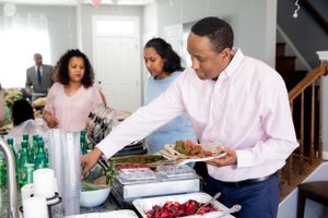 People serving food from a buffet line with drinks and appetizers at a celebration.