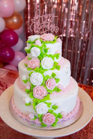Three-tiered white birthday cake decorated with pink and white roses and green leaves.
