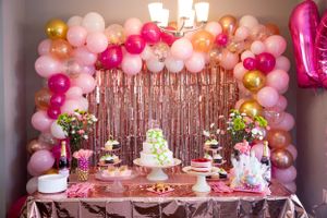 Pink and gold balloon arch decorating dessert table at festive party.