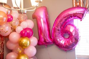 Pink number 16 balloon decorations with gold and pink party balloons arranged against a wall.