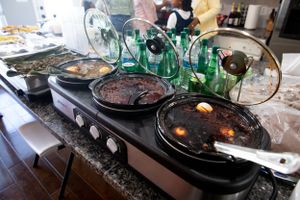 Multiple pans of food cooking on a stovetop with green glass bottles nearby.