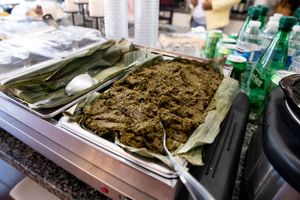 Large tray of prepared meat dish surrounded by serving utensils and green bottles.