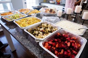 Catering buffet setup with various hot dishes in foil pans displayed on a granite countertop.