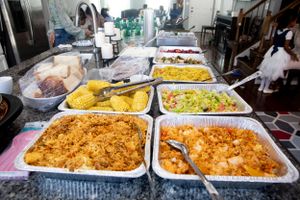 Large aluminum trays filled with colorful prepared foods in a commercial kitchen setting.