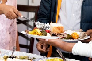 Hands serving plated meals with various colorful food items at a catered event.