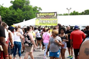 Crowd gathers near a smoothies and lemonade vendor stand at an outdoor festival.