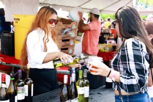 Vendor serves drinks to customer at outdoor festival wine tent.