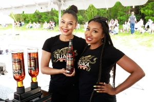Staff members in black uniforms displaying bottles at an outdoor beverage event.