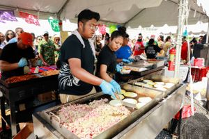 Food vendors preparing tacos at outdoor festival serving station.