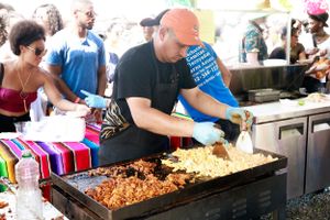 Food vendor grilling meat and preparing food at an outdoor festival stand.