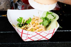 Fresh noodle dish garnished with cilantro and vegetables in a paper basket.