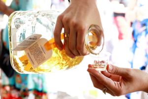 Hands pouring golden liquor from a bottle into a small glass.