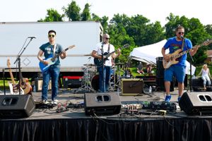 Band performing on stage with guitars and drum kit at an outdoor music festival.